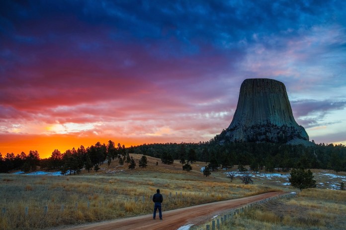 a lone hiker enjoys a dramtic sunrise over Devils tower national monument, WY