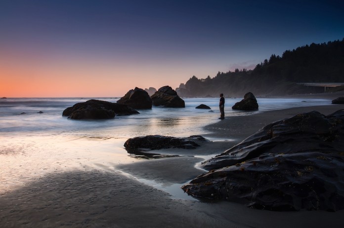 A silhouette of a photographer as dusk falls on the Pacific at Wilson Creek Beach
