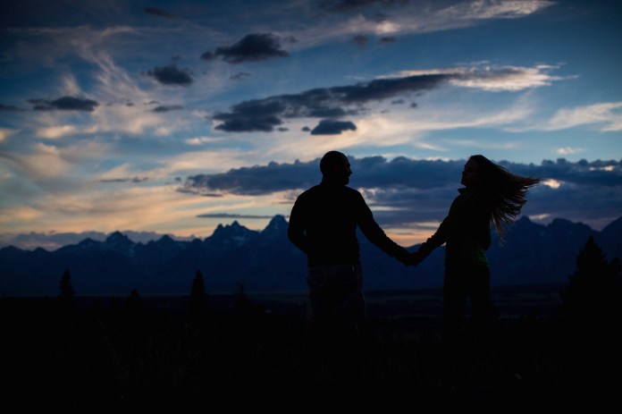 silhouette of a man and woman holding hands at dusk with the Tetons in the background